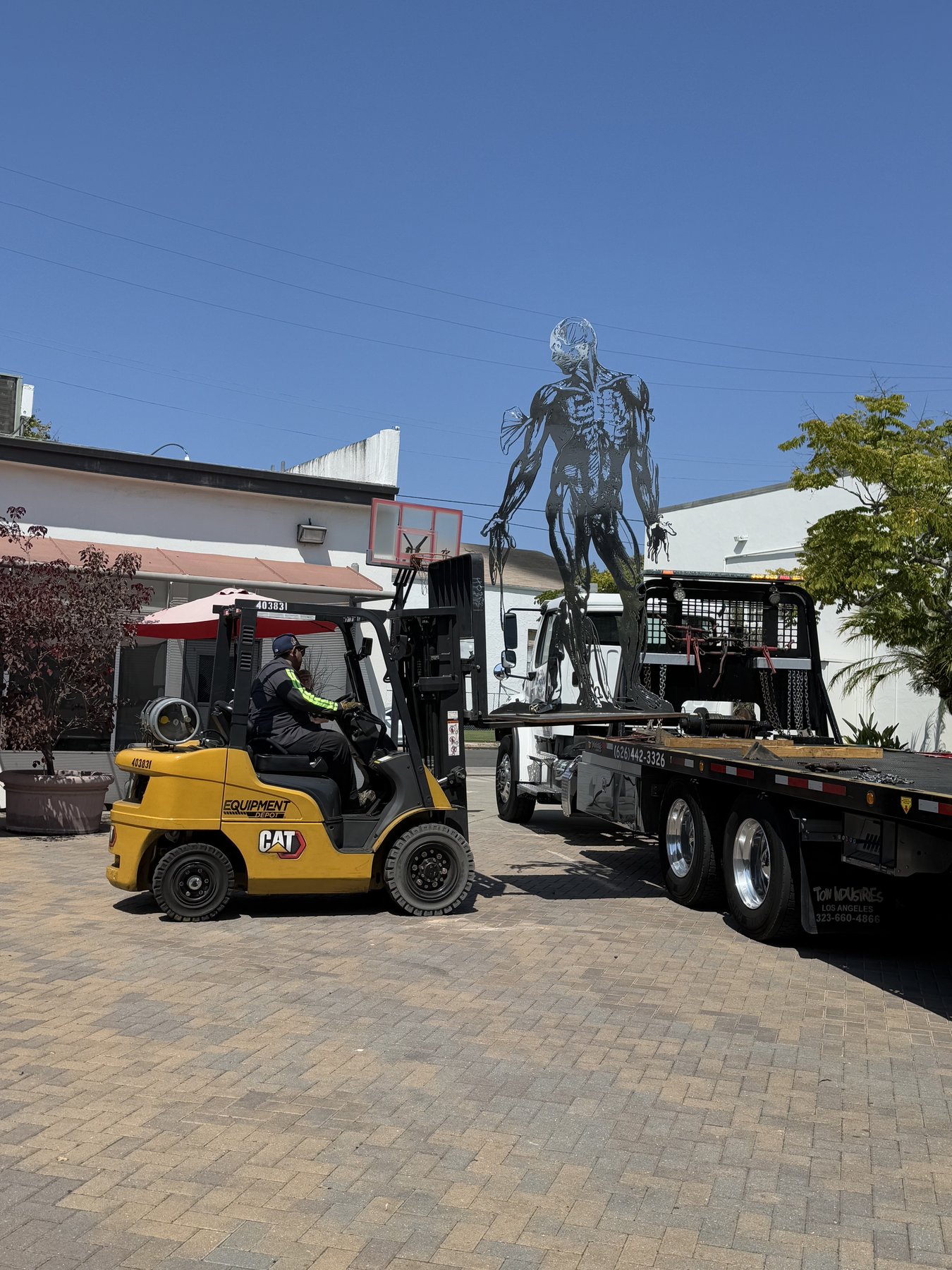 Cor Fabrica on a flatbed tow truck, sculpture standing upright while a forklift approaches to transfer it, July 24, 2025