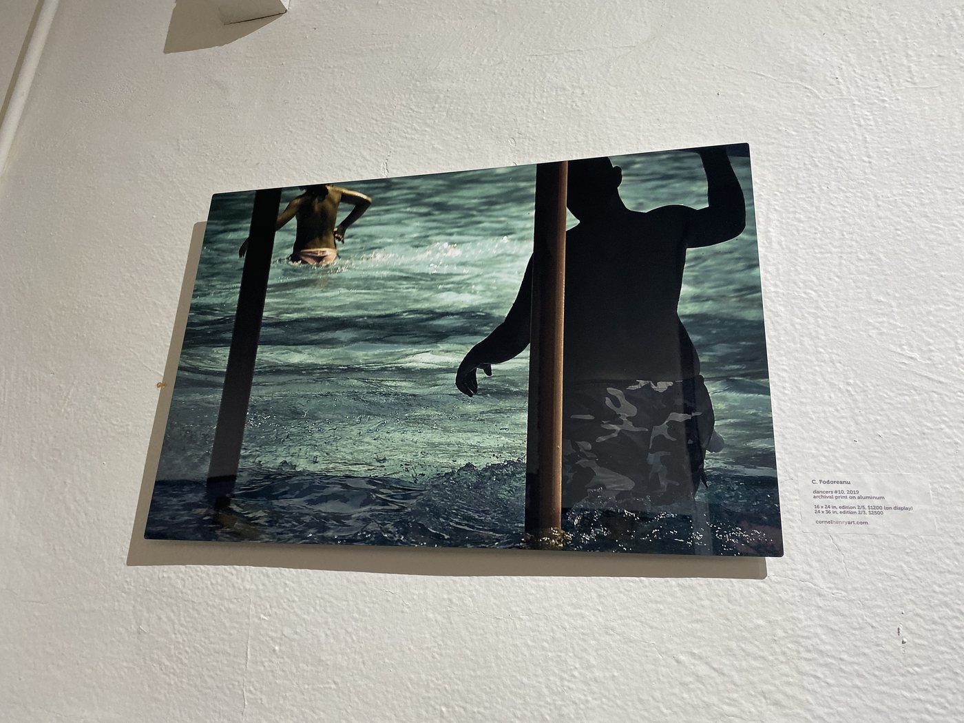 dancers, installation view at Cornel/Henry Art, San Diego, 2019 — a framed photograph of silhouetted figures by a pole in teal water, on a white wall
