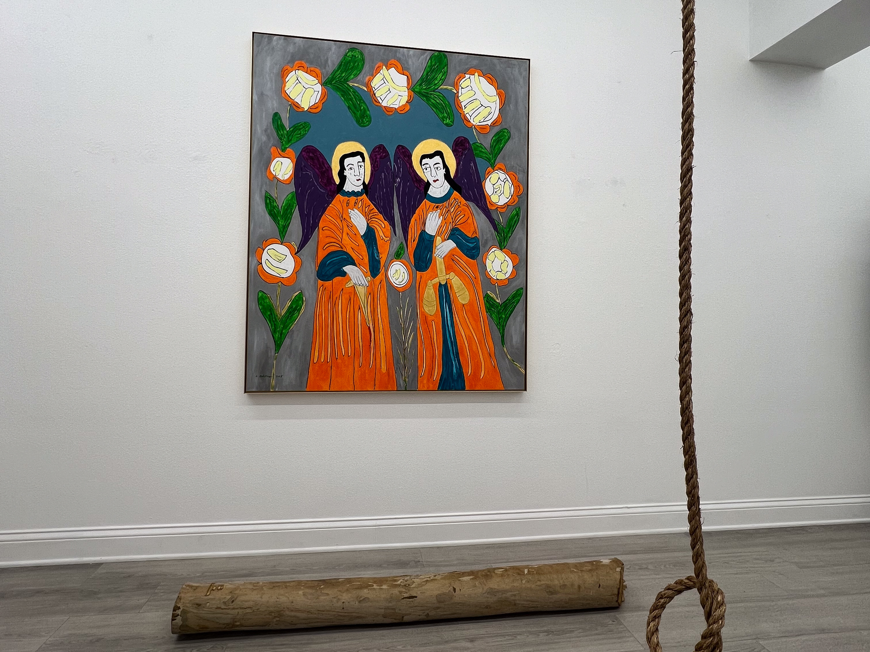 Archangels Michael and Gabriel by C Fodoreanu — large painting of two haloed angels in orange robes among stylized roses, installed on a white gallery wall with a fallen log and a hanging rope at right, from the writings exhibition at level of service not required.