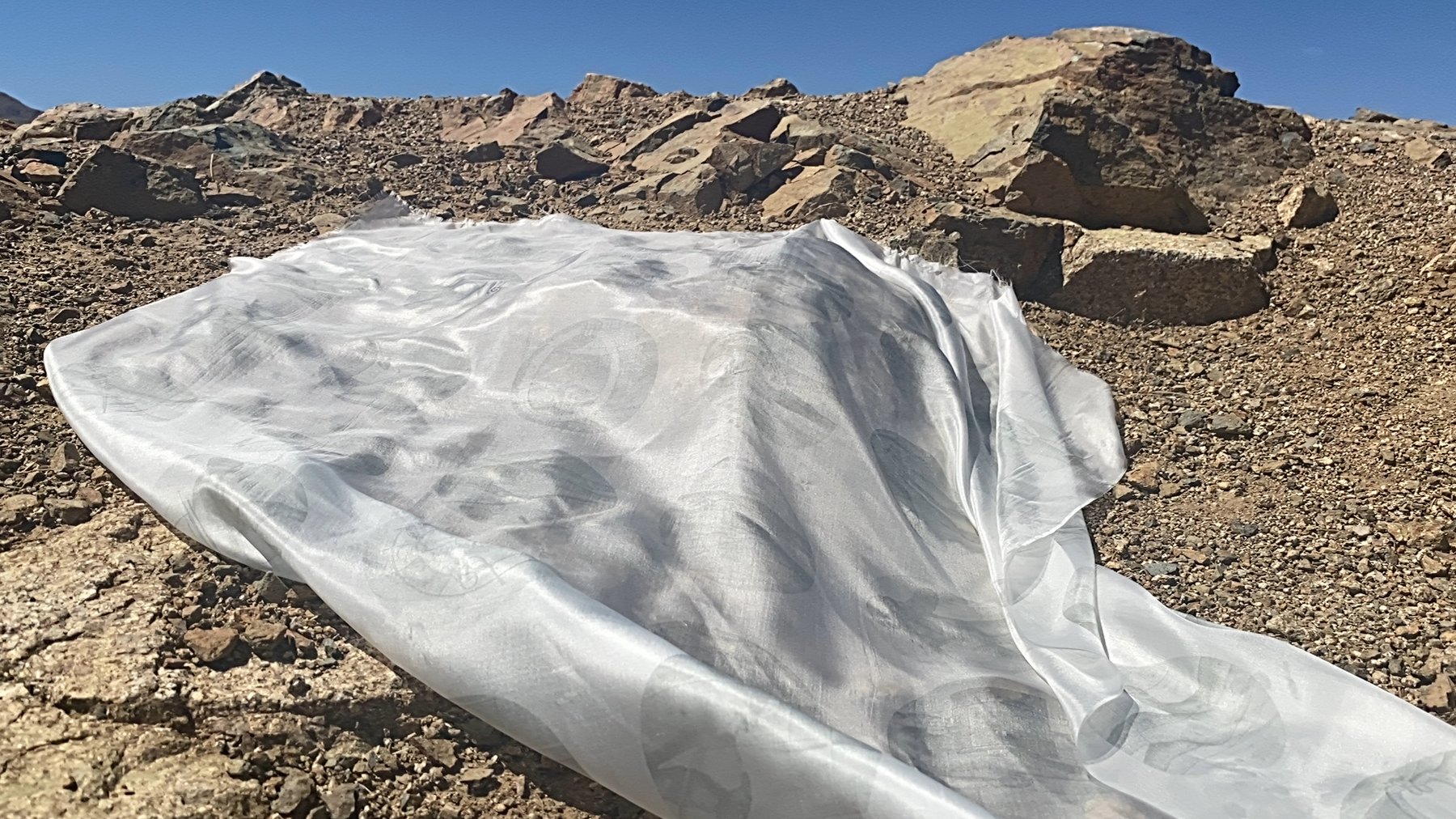 the white flag at Chocolate Drop, Twentynine Palms, CA, 2021 — silk fabric fallen across the rocky desert terrain, the printed body figures still visible