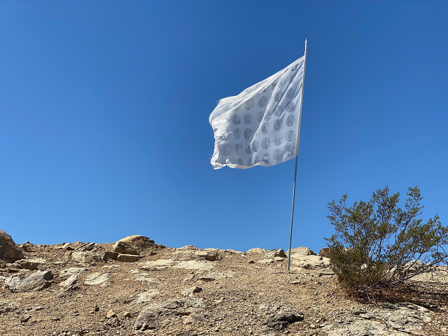 the white flag — silk flag bearing human-body imagery flying against a blue desert sky, 2021