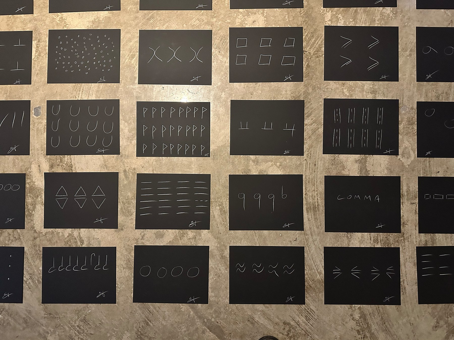 the giveaway, installation view at Ode to the Lake Sacalaia, Ronald H. Silverman Fine Arts Gallery, Cal State LA, 2023 — close-up of the floor grid revealing the chalk glyph vocabulary on individual panels: circles, U shapes, P shapes, the marks '9 9 9 b', 'COMMA', diamonds, and other proto-linguistic forms